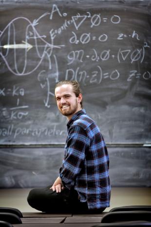 Ross Calvert, PhD Students, sitting in front of blackboard