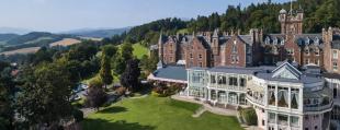 panoramic exterior view of Crieff Hydro Hotel with mountains, trees, fields and blue sky in the background