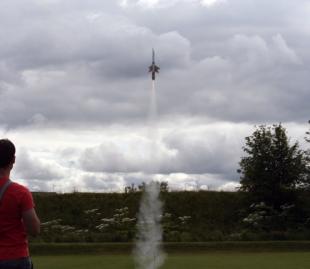 A home made rocket launching into the sky, taken from underneath looking up to the clouds