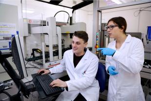 Postgraduate researchers wearing lab coats and viewing a monitor, in an engineering laboratory