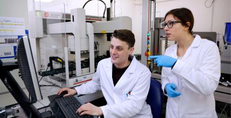 Postgraduate researchers wearing lab coats and viewing a monitor, in an engineering laboratory
